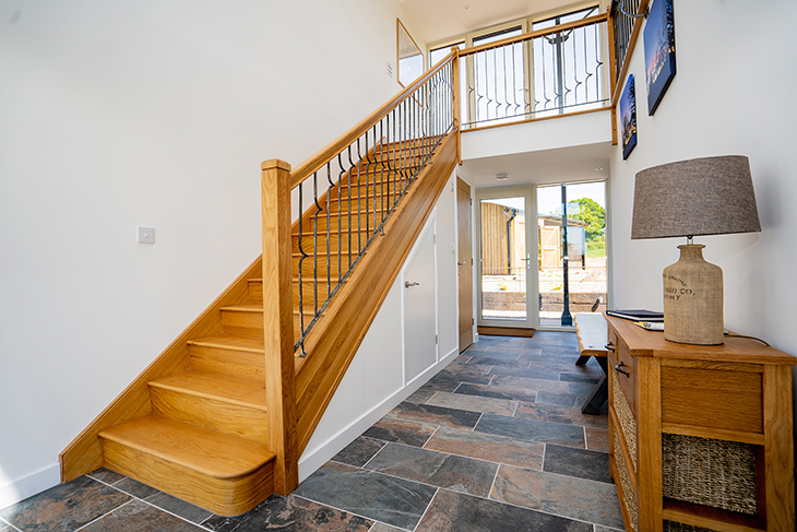 Hallway with oak stairs leading to living areas upstairs in this upside-down barn conversion by RRA Architects